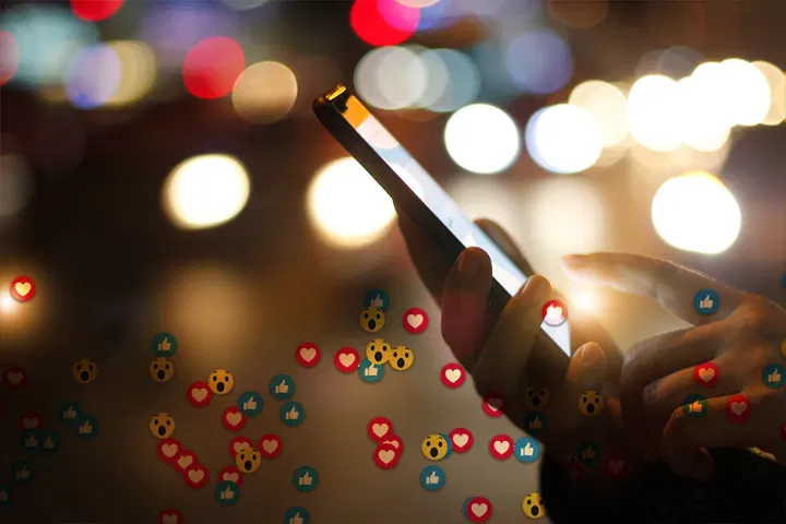 Phone with social engagement reactions against city lights